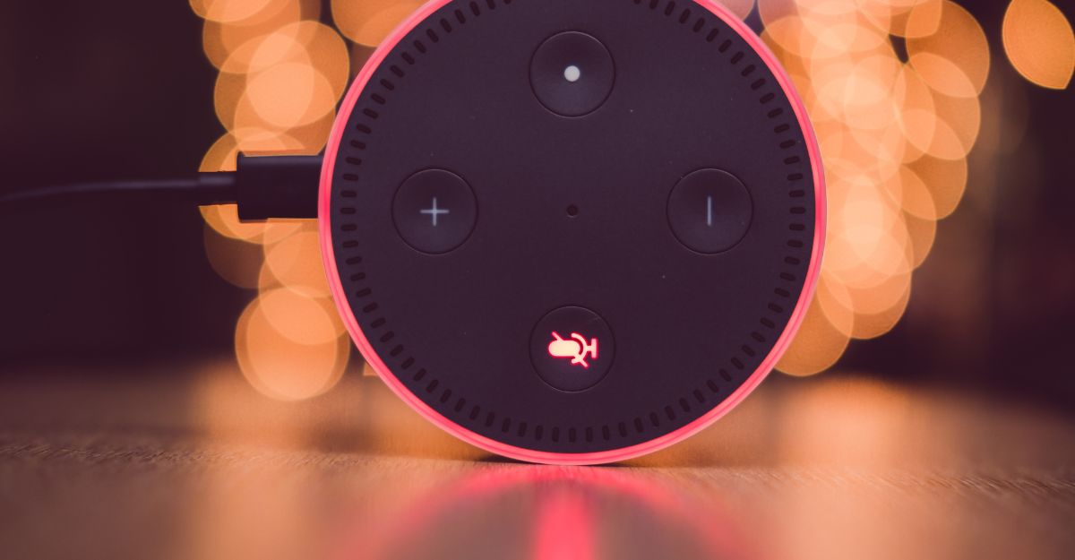 Imagem da Alexa xiaomi Echo Dot com microfone desativado, luz vermelha acesa e fundo desfocado com efeito bokeh quente.